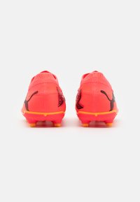 Scarpini da calcio di un vivace rosa acceso con tomaia sintetica testurizzata, dettagli neri e tacchetti arancioni. Presentano un design a profilo basso per maggiore agilità.