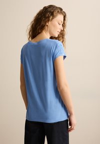 Camiseta de manga corta azul con cuello redondo y detalle fruncido en los hombros, hecha de una tela suave y lisa.