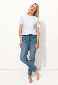 T-shirt blanc à manches courtes associé à un jean droit bleu clair. Le tissu semble lisse, et le jean présente des coutures visibles et des poches.