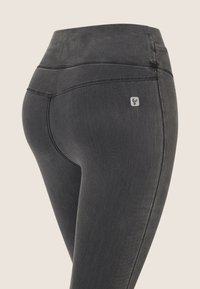 Leggings neri a vita alta con una texture liscia, dettagli di cucitura e un piccolo logo sulla parte posteriore. Design aderente e materiale elasticizzato.