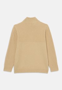 Beige ribbesweater med høy krage, med teksturert strikk på den øverste delen og glatt stoff på den nederste halvdelen. Lange ermer.