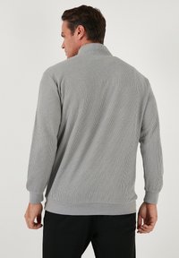 Gray ribbed pullover with a high collar, long sleeves, and a straight hem. Features a textured fabric and cuffed sleeve ends.