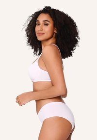 Bra bianco in morbido tessuto con spalline regolabili, abbinato a mutande bianche seamless coordinate. Texture liscia, design minimale.