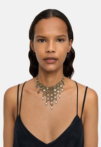 Naszyjnik choker w kolorze złotym z akcentami srebrnymi, z okrągłymi i diamentowymi zdobieniami, wykończony lustrzanymi powierzchniami.