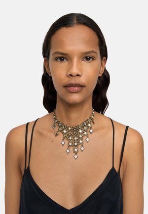 Naszyjnik choker w kolorze złotym z akcentami srebrnymi, z okrągłymi i diamentowymi zdobieniami, wykończony lustrzanymi powierzchniami.