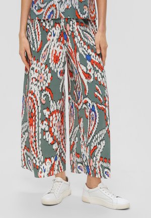 Pantalon large à motifs floraux de longueur jambe en vert, blanc, orange, bleu et rose, porté avec des baskets blanches sur une personne.