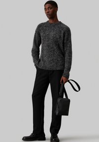 Suéter gris texturizado con cuello redondo, combinado con pantalones negros y un pequeño bolso negro, que presenta un diseño sencillo y una correa ajustable.