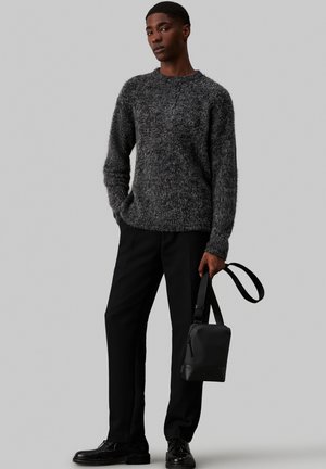 Maglione grigio a trama con collo rotondo abbinato a pantaloni neri e una piccola borsa nera, che presenta un design semplice e una tracolla regolabile.