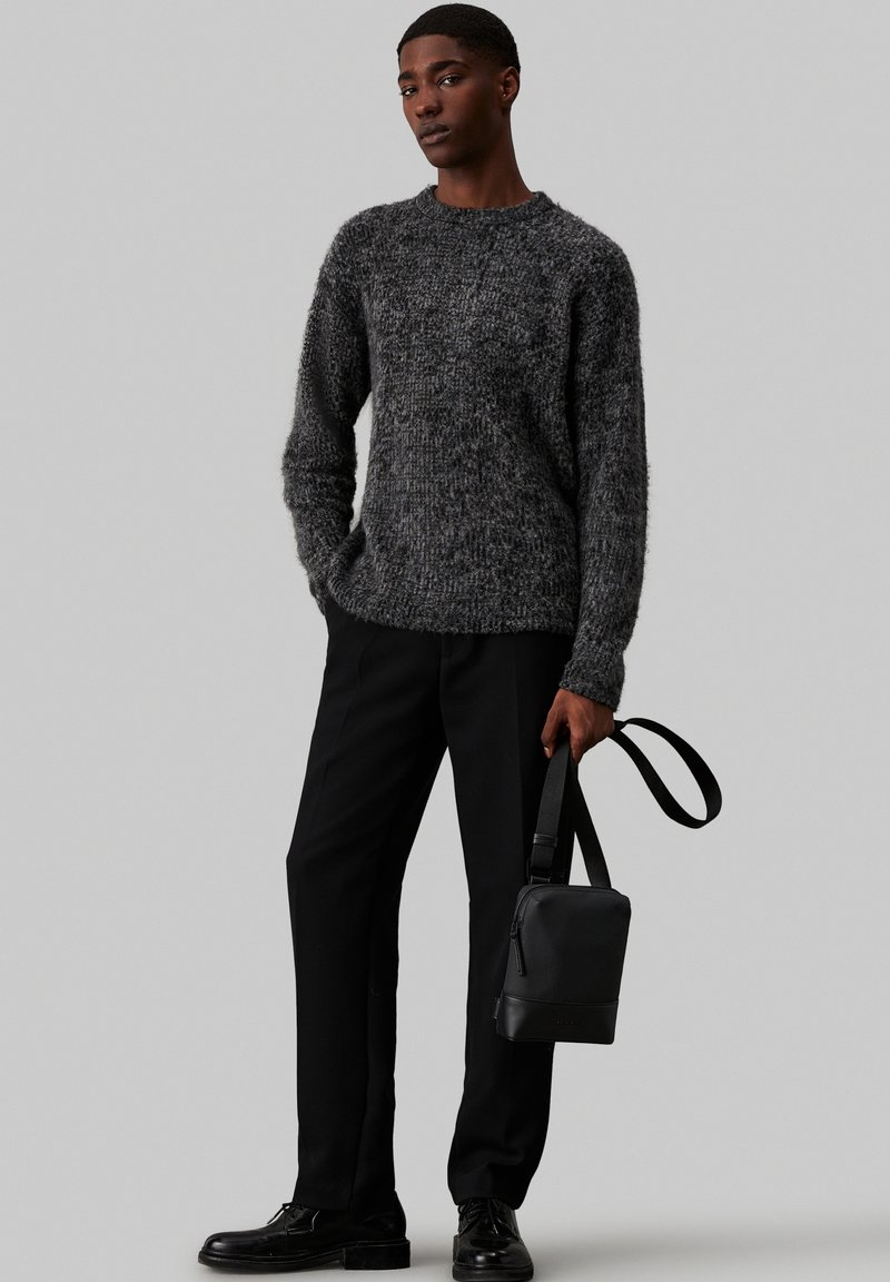 Suéter gris texturizado con cuello redondo, combinado con pantalones negros y un pequeño bolso negro, que presenta un diseño sencillo y una correa ajustable.