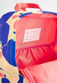 Zaino con un motivo floreale colorato, caratterizzato da un interno rosa brillante, un'etichetta con nome e una tasca con zip con fodera arricciata.