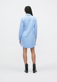 Lichtblauwe overhemdjurk met lange mouwen, knoopmanchetten en een gebogen zoom. Gemaakt van gladde stof, met een klassieke kraag en een rugpand.