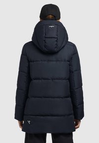 Navy blue puffer coat with a hood, featuring quilted sections, an elastic drawstring, and a logo patch near the hem. Smooth texture.