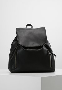 Sac à dos en cuir noir avec couvercle à rabat, doté de deux fermetures éclair latérales et d'une poignée supérieure. Texture lisse, design simple et forme structurée.