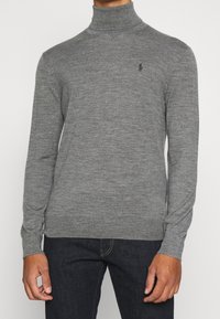 Grå turtleneck-tröja gjord av mjukt tyg, med långa ärmar och en smal passform. Litet logo broderat på bröstet.