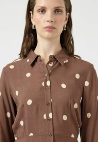 Brązowa koszula na guziki z kołnierzykiem, ozdobiona dużymi kremowymi groszkami i długimi rękawami, wykonana z gładkiego materiału.