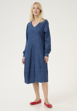 Jeansklänning i blått, knälång med långa puffärmar och V-ringning. Har en söm ner i mitten och en sydd fåll. Röda ballerinaskor.