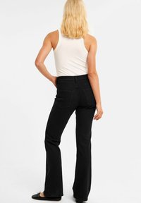 Svarta utsvängda jeans med hög midja, tillverkade av denim, med två bakfickor och en slät yta. Bärs med en vit linne.