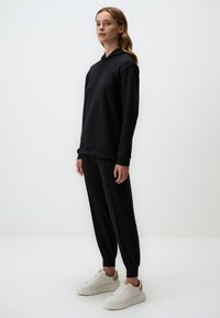 Zwarte hoodie en bijpassende joggers van zachte stof, met een relaxte pasvorm en ribgebreide boorden, gecombineerd met witte sneakers.