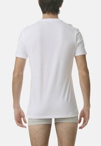 Biała koszulka z krótki rękawem i okrągłym dekoltem, wykonana z gładkiego materiału, noszona na jasnoszarym bieliźnie. Minimalistyczny design bez widocznych logo.