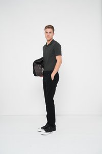 Mustra musta lühikese varrukaga polo särk, tumedad slim-fit püksid ja mustad tenningud valge tallaga. Mudel hoiab tumedat kotti, poseerides valge tausta ees.