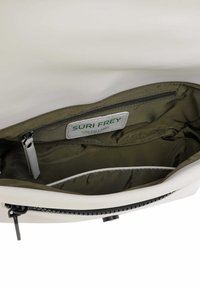 Interior de una bolsa blanca que muestra un forro verde oliva, un compartimento con cremallera y una etiqueta que dice "SURI FREY GREEN LABEL."
