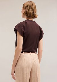 Top marrone a maniche corte con scollo rotondo, abbinato a pantaloni beige chiaro a righe e una cintura marrone. Tessuto morbido.
