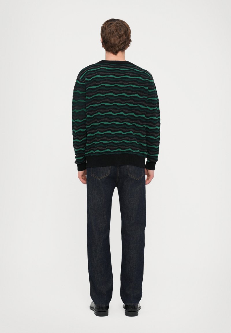 Black sweater with green and gray wavy pattern; features ribbed cuffs and neckline. Worn with dark blue denim jeans and black shoes.