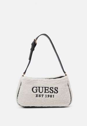 Vit plyschhandväska med svart läderrem och guldfärgade detaljer. "GUESS EST 1981" är broderat i svart på framsidan. Rektangulär form.