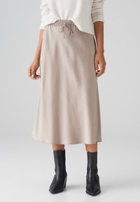 Beige Midikleid mit elastischem Bund und Kordelzug, aus glattem Stoff gefertigt. Kombiniert mit schwarzen Knöchelstiefeln.