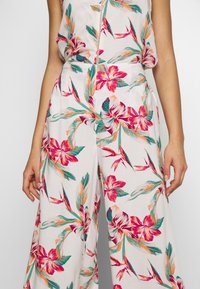 Pantalons larges imprimés floraux en tissu léger. Présentent des fleurs roses vives, orange et turquoise sur un fond blanc. Détails de pinces.