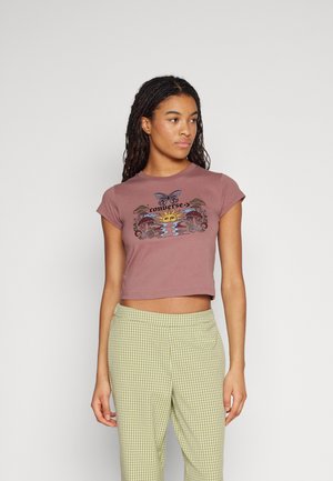 Camiseta corta de color malva con un gráfico de mariposa y sol, adornado con acentos florales. Combinada con pantalones de cuadros verdes de cintura alta.