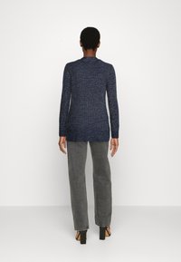Maglione blu navy a maglia con maniche lunghe e scollatura a barca, con bordo a coste. Abbinato a pantaloni grigi a gamba dritta e tacchi open-toe.