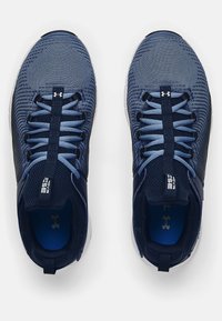 Marina idrottsskor med en texturerad mesh-överkropp, kontrasterande blå detaljer, en vadderad innersula och en flexibel vit sula. Snörningarna är ordentligt knutna.