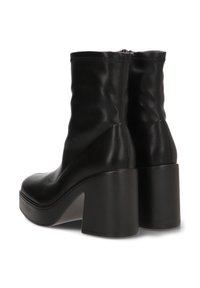 Botines de cuero negro con un acabado suave, que cuentan con un tacón grueso y un caño ajustado, mostrando detalles de costura mínimos.