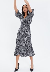 Vestido negro con lunares blancos, mangas cortas abullonadas, escote en v, cintura ajustada, dobladillo acampanado y un borde con volantes en la parte inferior.