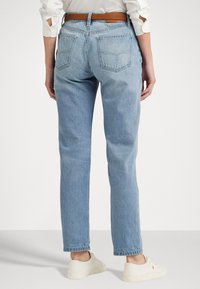 Lichtblauwe denim jeans met een rechte snit, vijf zakken en een bruin leren riem die de taille accentueert. Zachte textuur en klassieke afwerking.