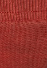 Punainen ribbipintainen kangas, jossa on pehmeä tekstuuri ja näkyvät saumat, esittelee tasaisen kuvion ja johdonmukaisen värityksen kauttaaltaan.