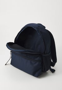Zaino blu navy realizzato in tessuto resistente, con una grande apertura, tasca frontale con zip e tasca laterale in rete per ulteriore spazio di stoccaggio.