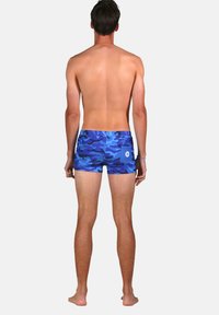 Shorts de bain camouflés bleus avec une coupe ajustée, une taille élastique et une poche arrière. Le matériau semble lisse avec une texture légère.