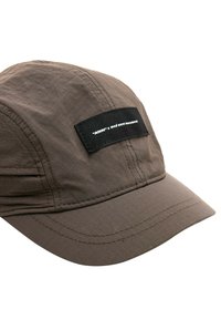 Gorra marrón con una tela texturizada, visera curvada y una etiqueta negra con texto blanco en el frente. Detalles de costura visibles.