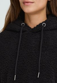 Sort fleece hoodie med struktureret stof, der har en hætte, justerbare snore med sølv-punkter og en afslappet pasform.