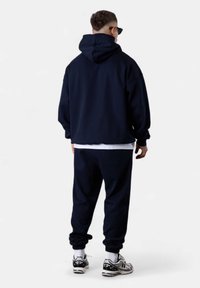 Navyblauer Hoodie und passende Jogginghosen aus weichem Material, mit lockerer Passform, Kapuze und elastischen Bündchen, kombiniert mit sportlichen Schuhen.