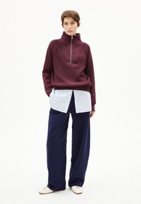 Bordeaux geribbelde trui met hoge kraag en rits, gelaagd over een lichtblauw overhemd met knopen, gecombineerd met marineblauwe wijdvallende broek.