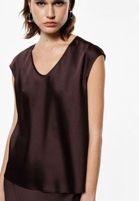 Top in satin marrone scuro con scollatura a V e maniche corte. Texture liscia; vestibilità rilassata con orlo leggermente curvo.