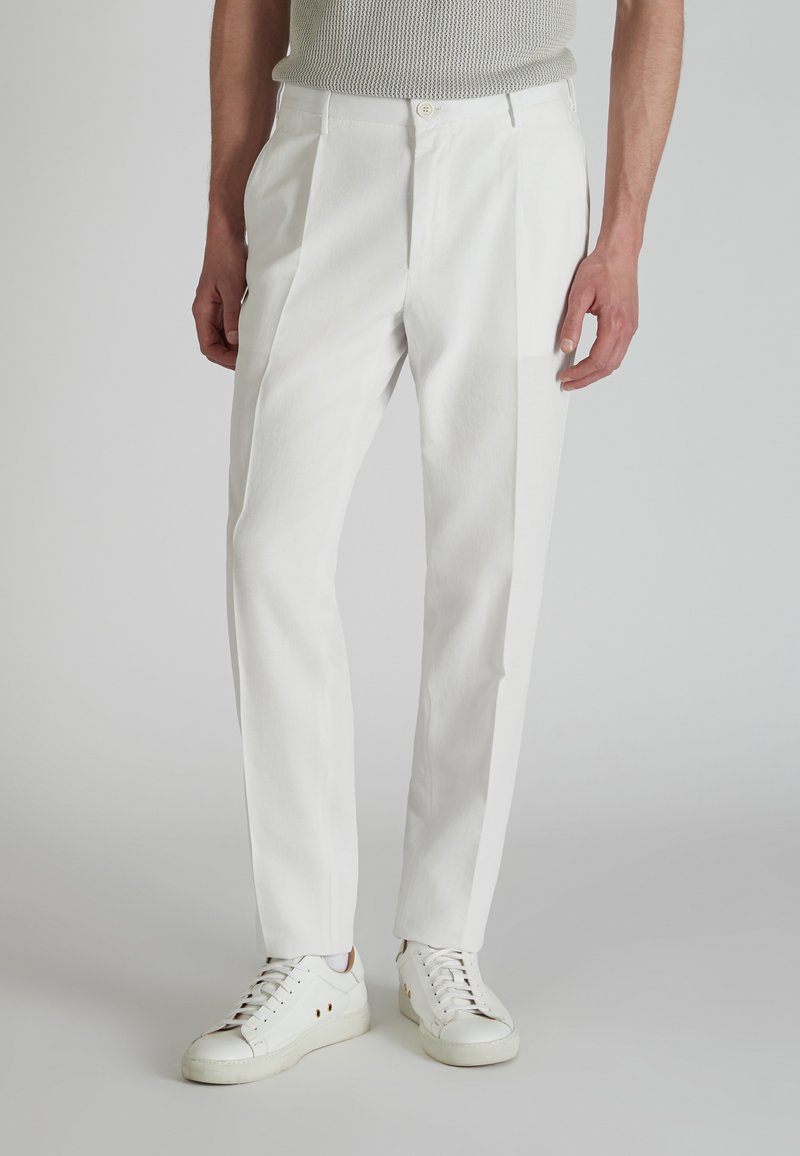 Pantalones blancos de talle alto con una textura suave, que presentan pliegues y bolsillos laterales, combinados con zapatillas blancas.