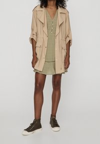 Beige oversized jacket with rolled sleeves, layered over a light green checked dress, paired with olive high-top sneakers.