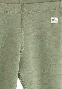 Grønne leggings i blødt stof med en glat tekstur, featuring et lille mærke med et regnbue-design nær taljen.