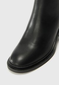 Stivale alla caviglia in pelle nera con texture liscia, punta arrotondata e suola nera sollevata con dettagli di cucitura discreti.