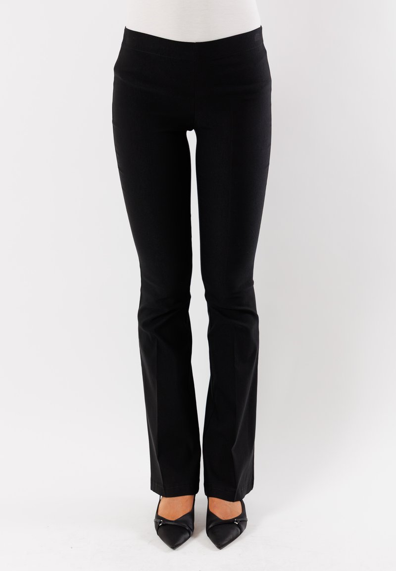 Pantaloni neri aderenti con una texture liscia, vita media, gambe svasate e un design pulito, indossati con tacchi a punta neri.