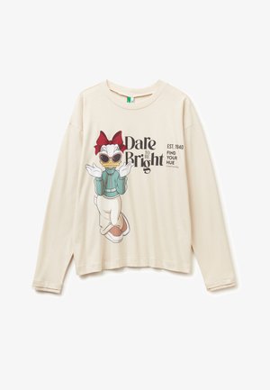 Camisa de manga larga crema con un pato de dibujos animados usando gafas de sol, pajarita roja, chaqueta verde; texto "Atrévete a ser Brillante," "Est. 1940," "Encuentra tu Tono."